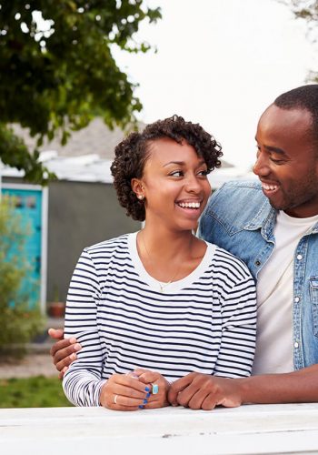Couple standing in front of home, smiling at each other