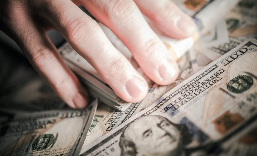 Man's hand touching hundreds of dollars