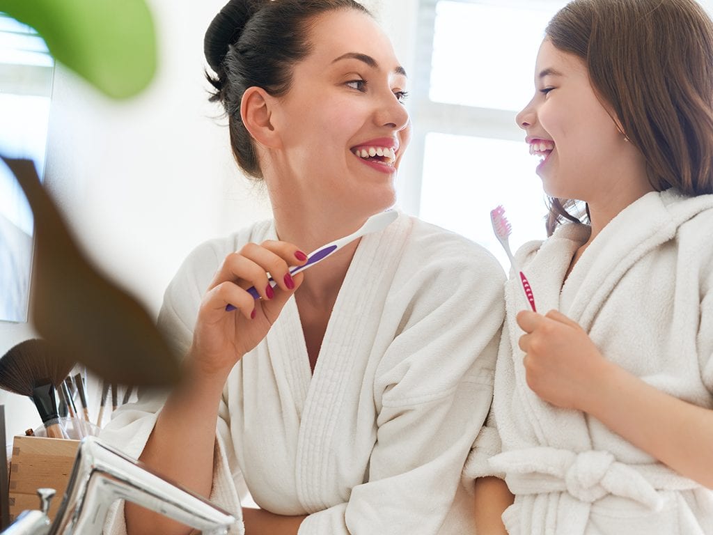 Mom and daughter looking at each other smiling and holding toothbrush