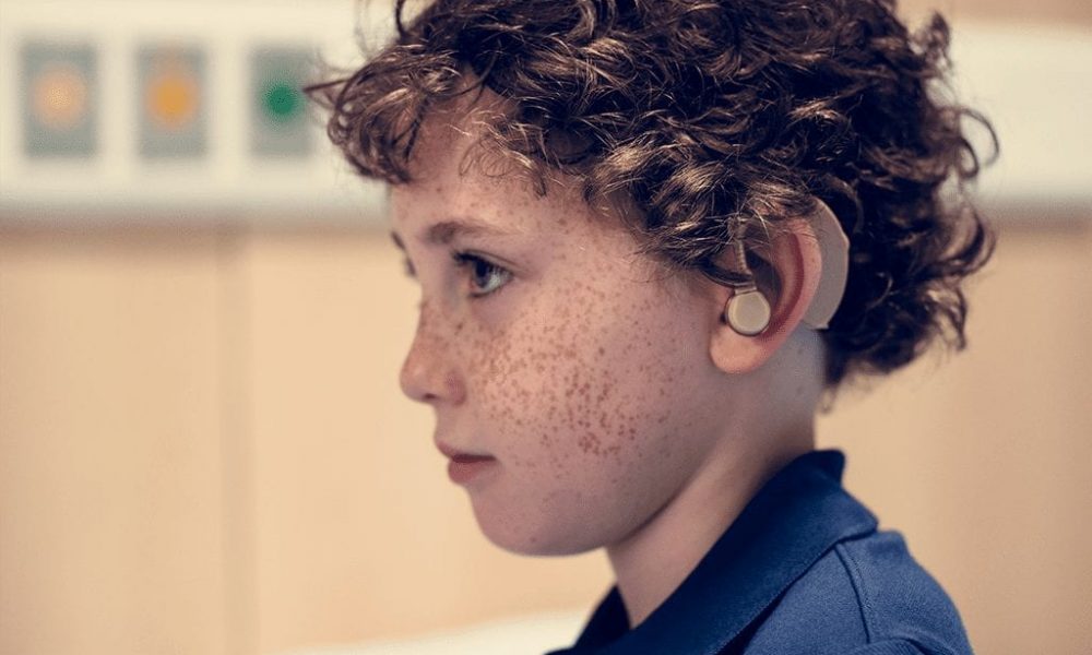 Side profile of brown curly haired kid with hearing aid in left ear