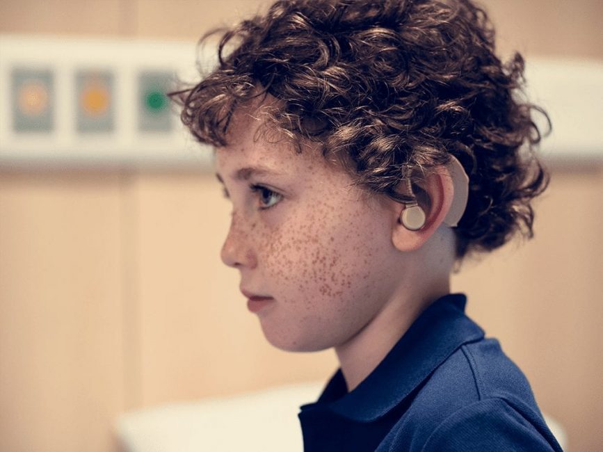 Side profile of brown curly haired kid with hearing aid in left ear