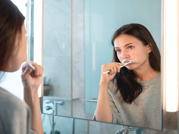 Girl Brushing Teeth Dark haired girl in grey sweater looking in mirror brushing her teeth