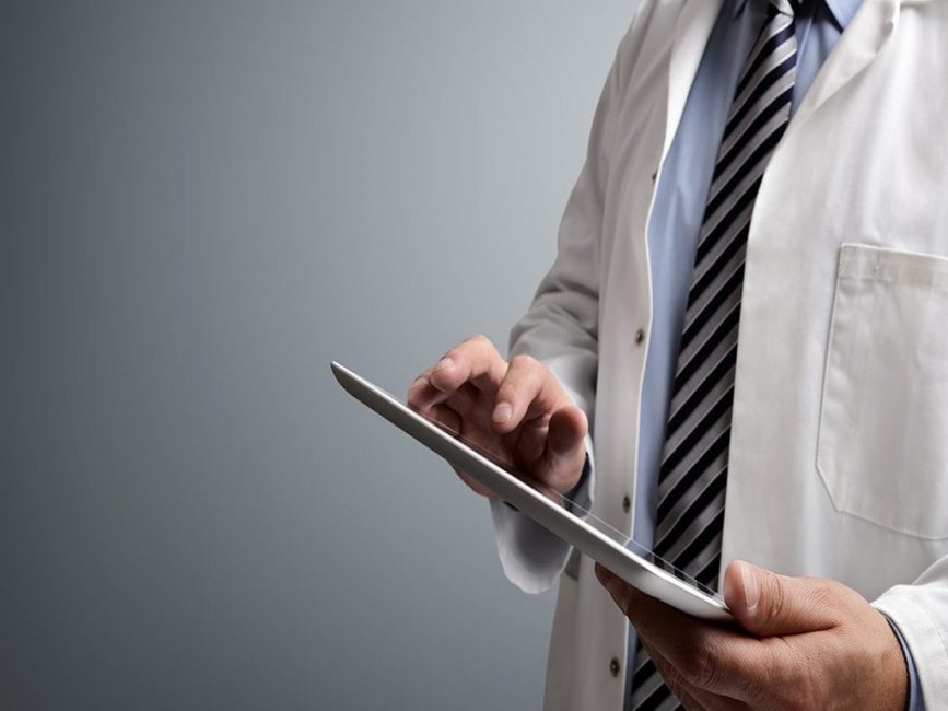Doctor in lab coat and stripped tie working on tablet