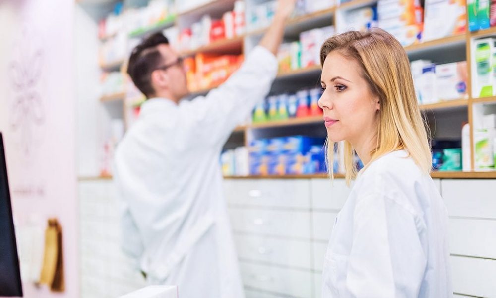 Pharmacist reviewing medications with co-worker in the background