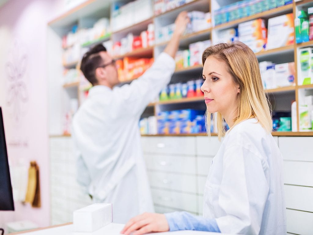 Pharmacist reviewing medications with co-worker in the background