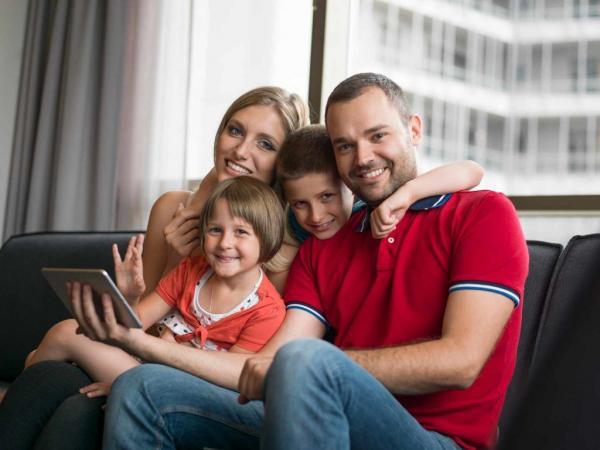 Family sitting on couch Mom, dad, boy and girl sitting on the couch looking at a tablet