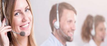 Call center girl smiling at camera with head set in place and guy faded out in the background