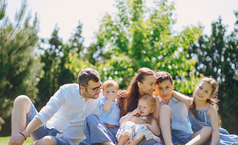 Husband, wife and four kids in a green grassy field hugging on one another