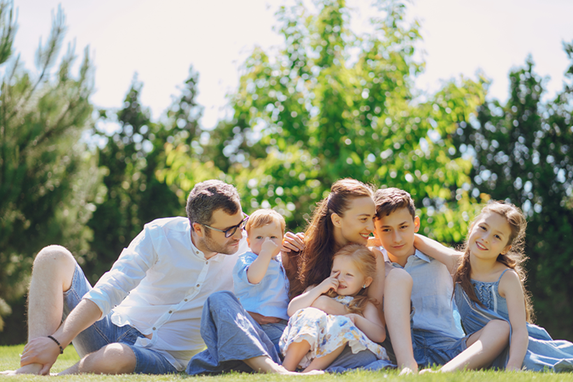 Husband, wife and four kids in a green grassy field hugging on one another