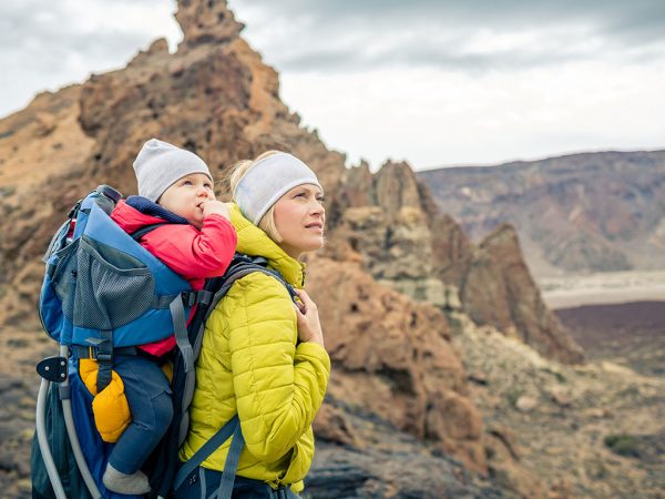 Mom carrying baby on her back in hiking pack walking through the mountains