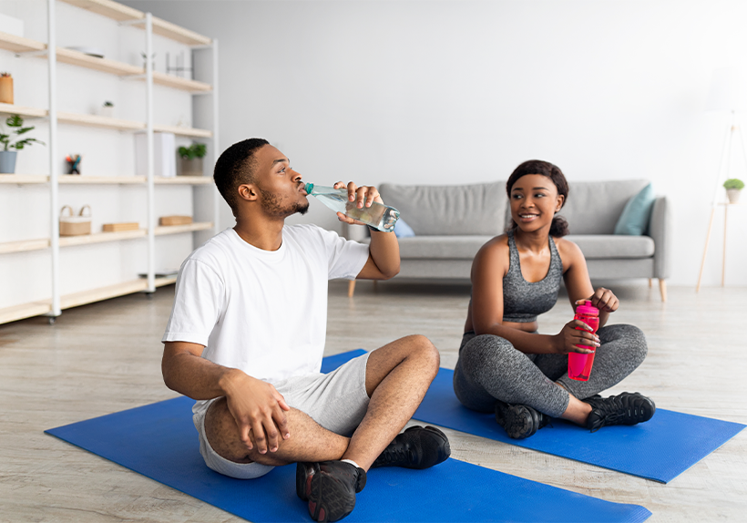 an African American male and female athlete drinking water staying hydrated